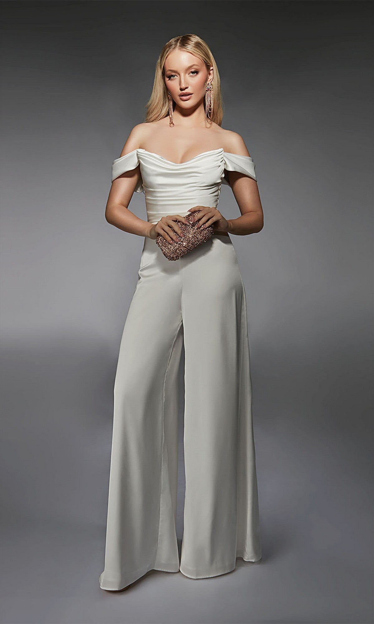 A woman poses against a gray background, wearing the Alyce 70071 long formal jumpsuit in ivory with wide-leg pants, and holds a sparkly clutch bag.